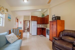 A living room with a sofa, a dining table, and a kitchen area with wooden cabinets and appliances. - Oceanfront Casita w/pool-kayaks-paddleboards-beach (San Pedro)