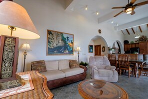 A spacious living area with a sofa, armchairs, a coffee table, and a painting of a tropical scene. - Beachfront Estate pool/kayak/paddleboard Sleeps 12 (San Pedro)
