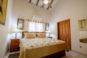 A bedroom with a bed, two bedside tables, a wooden door, an air conditioning unit, and a ceiling fan. - UPPER 2BR/2BA Oceanfront w/Pool/kayak/paddleboards (San Pedro)