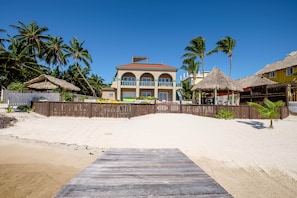 A beachfront property with a wooden deck leading to a building with multiple balconies and a thatched-roof structure. - UPPER 2BR/2BA Oceanfront w/Pool/kayak/paddleboards (San Pedro)