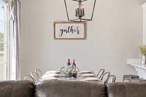 Ein Essbereich mit einem Tisch für vier Personen, einer Chandelüster und einem Schild mit der Aufschrift 'gather'.