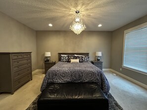 A bedroom with a large bed, two bedside tables with lamps, a dresser, a chandelier, and a window with blinds. - Aspen Place | Zero-Step, 2 En-Suites, 1.5mi Mayo (Rochester)