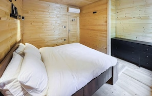 Una habitació de fusta amb un llit, un taulell negre i una paret de fusta amb una porta.