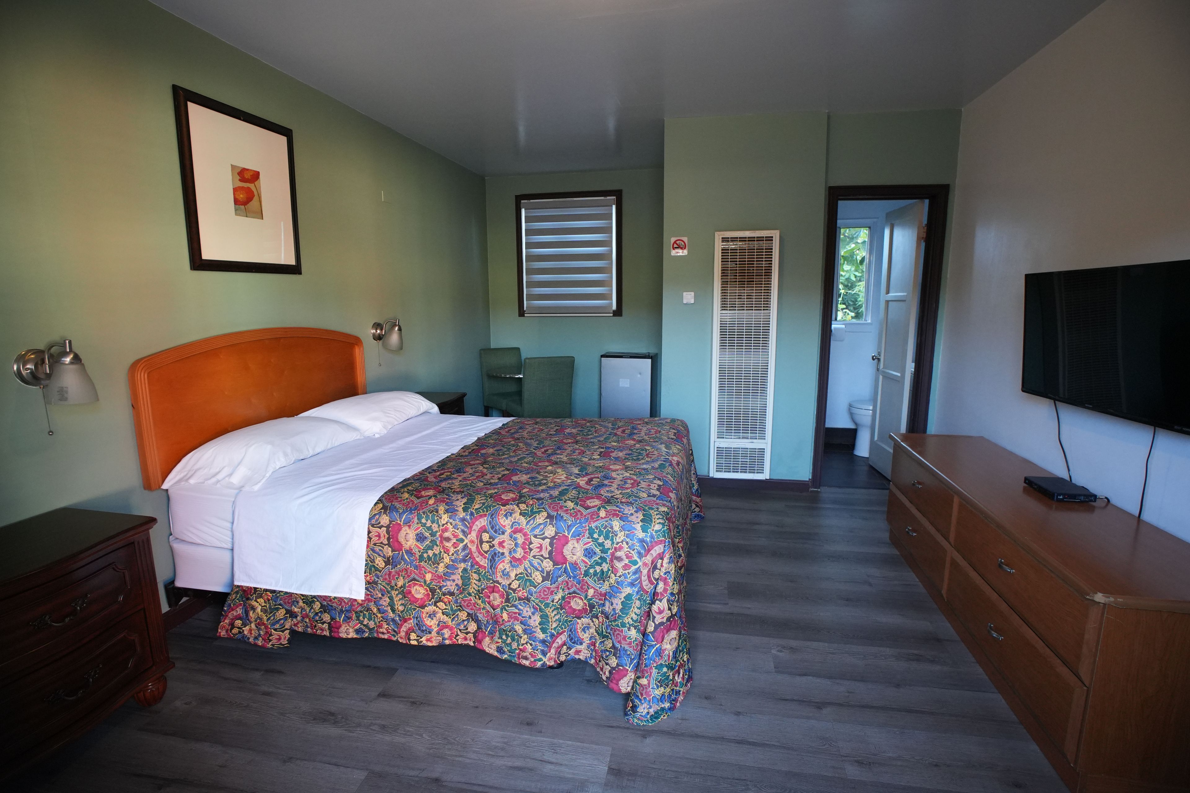 A bedroom with a bed, dresser, television, and a door leading to a bathroom.