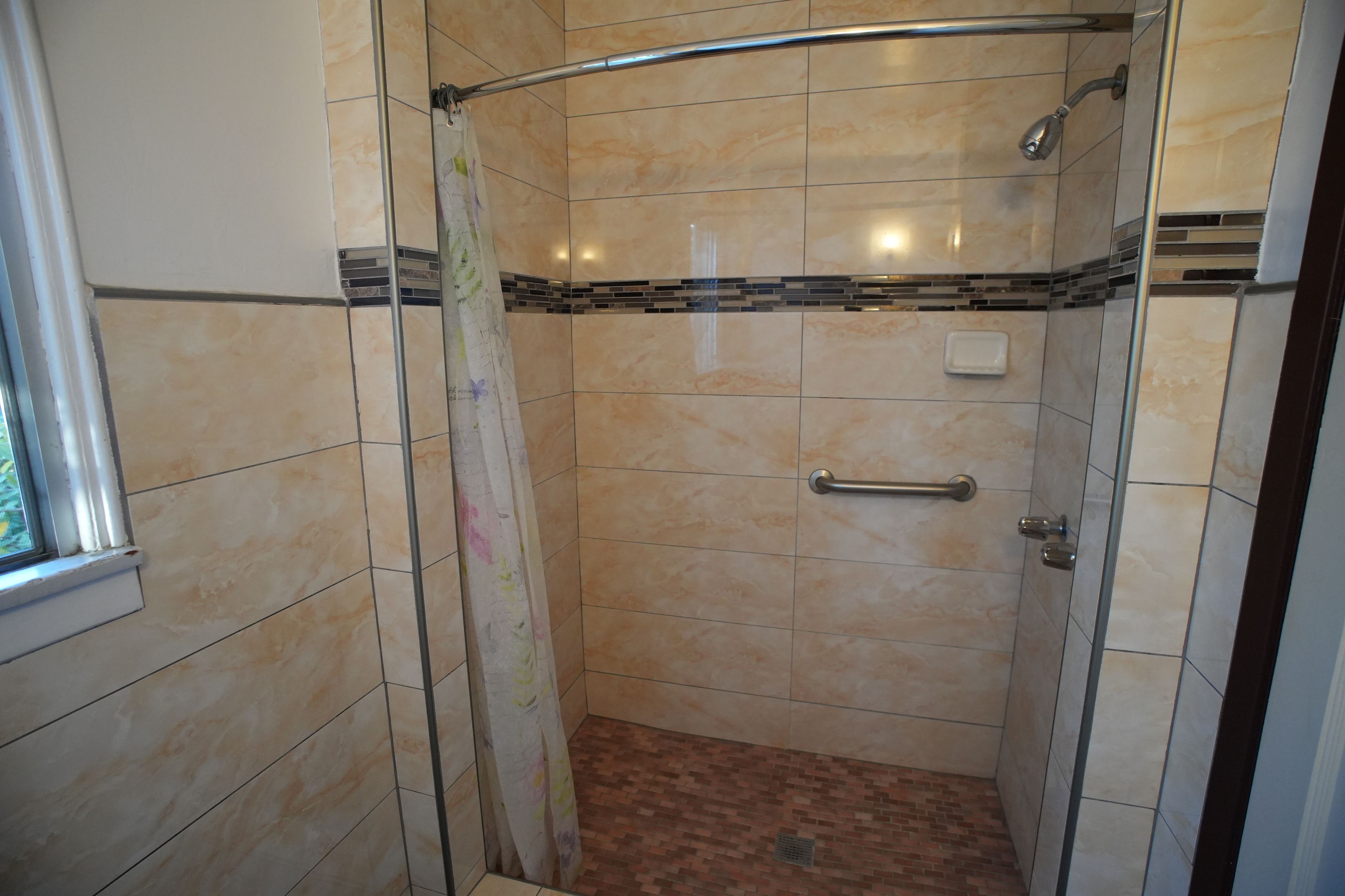 A shower with a glass door, a handrail, and a tiled floor.