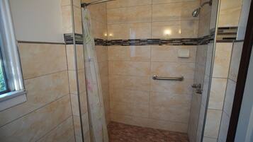 A shower with a glass door, a handrail, and a tiled floor.