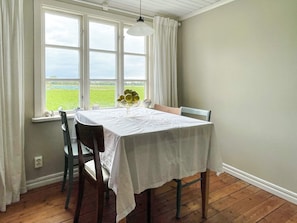 A dining area with a table set for two, a window with curtains, and a view of a green field. - 8 Person Holiday Home in Lottorp (Löttorp)
