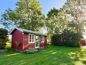 A small red wooden building with a green door and windows, surrounded by a well-maintained lawn and trees. - 8 Person Holiday Home in Lottorp (Löttorp)