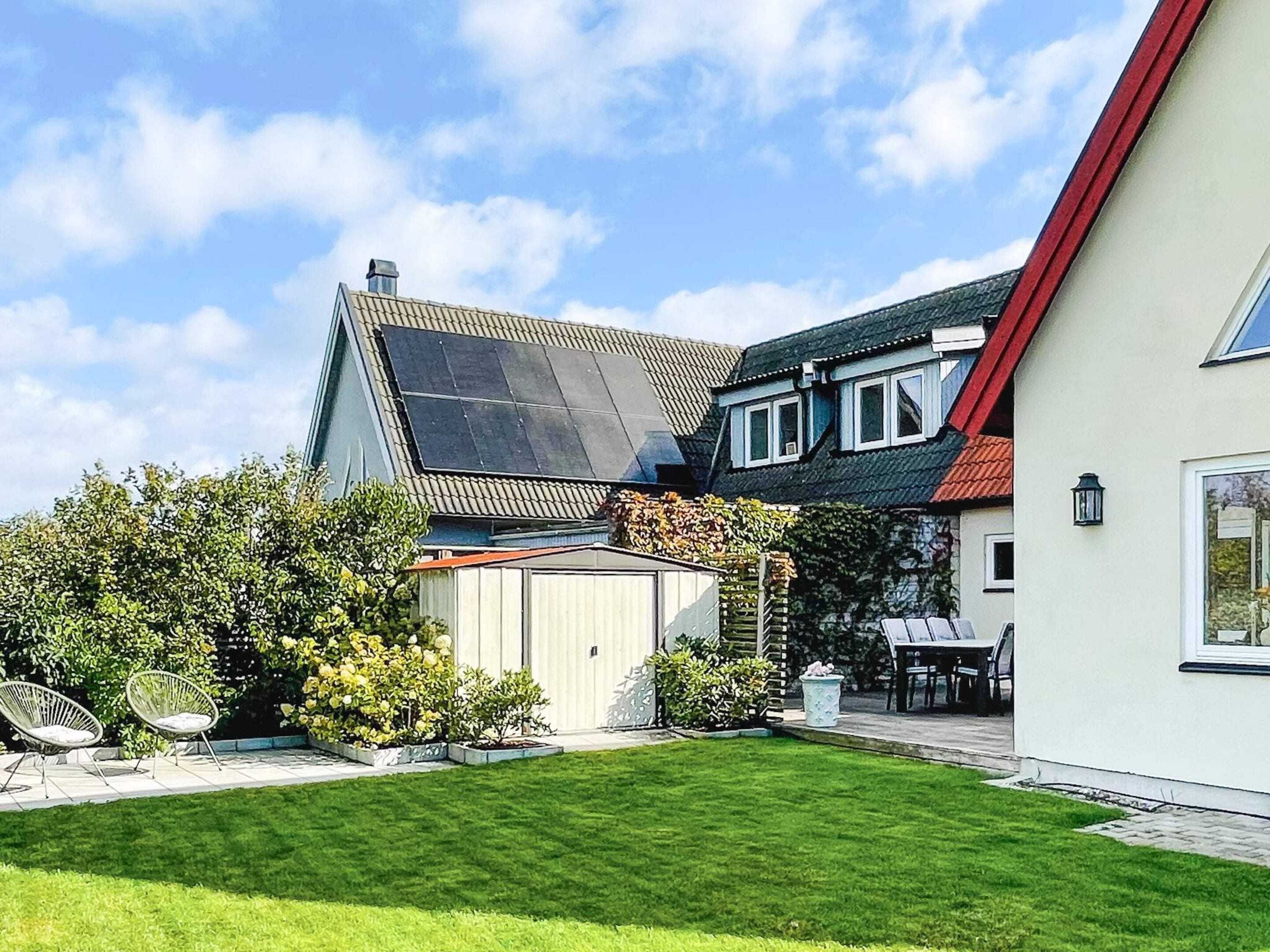 Et moderne hus med sadeltag, solpaneler, en velholdt græsplæne og udendørs møbler.