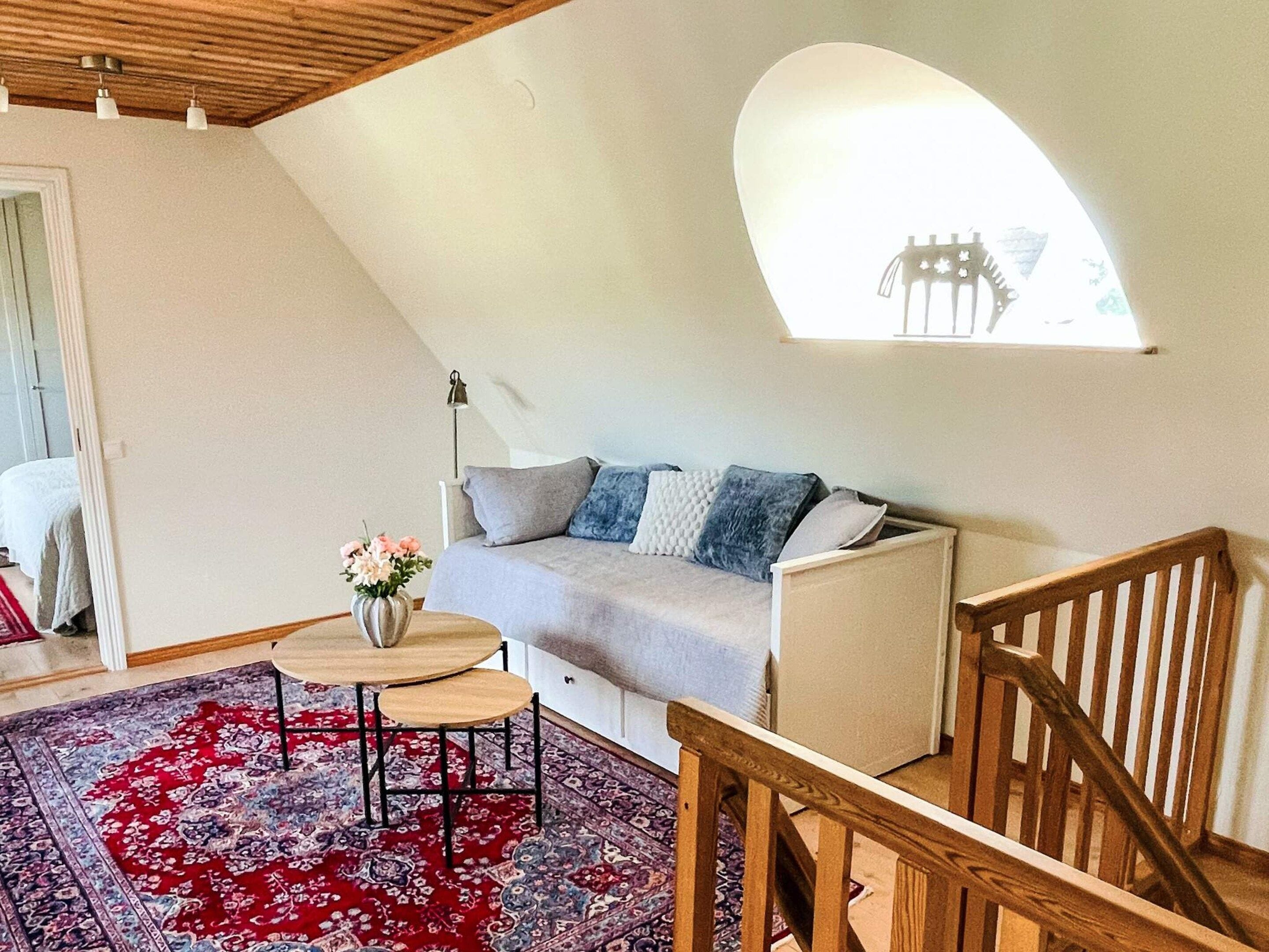 Et hyggeligt værelse med skråvægge, en sofa, et lille bord med en vase og en tæppe med et mønster.