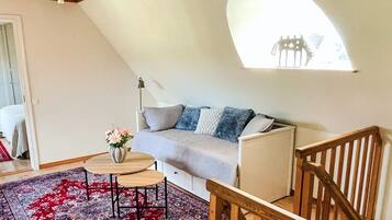 Et hyggeligt værelse med skråvægge, en sofa, et lille bord med en vase og en tæppe med et mønster.