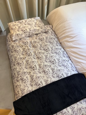 Ein Bett mit einem blumigem Bettbezug und einem schwarzen Kopfkissen.