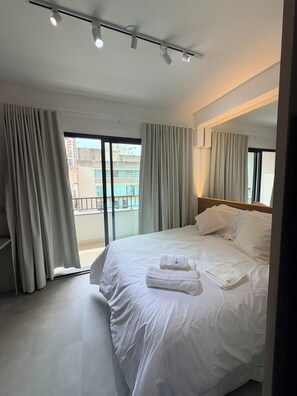 Ein Hotelzimmer mit einem großen Bett, Vorhängen, einem Balkon und Blick auf Gebäude.