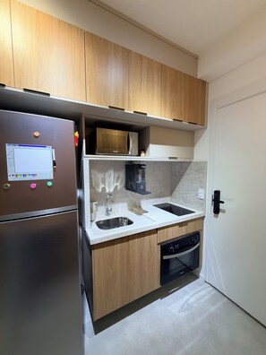 Eine kleine Küche mit Holzausstattung, einem Edelstahlkühlschrank, einer Mikrowelle, einem Spülbecken und einem Geschirrspüler.