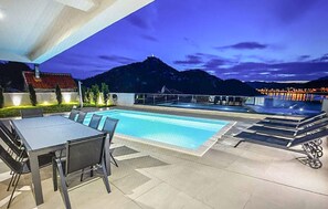An outdoor swimming pool with a dining area and lounge chairs, surrounded by mountains and a night sky. - Beautiful home in Rogotin with private swimming pool, can be inside or outside (Rogotin)