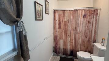 A bathroom with a wooden shower curtain, a toilet, a sink, and a window with a towel hanging.
