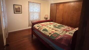 A bedroom with a wooden bed, a window with curtains, a ceiling light, and a door.