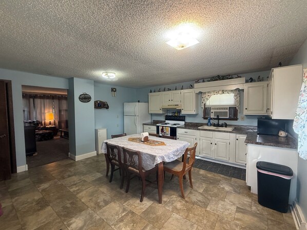 A compact kitchen with a dining area, a refrigerator, a stove, and a trash bin.