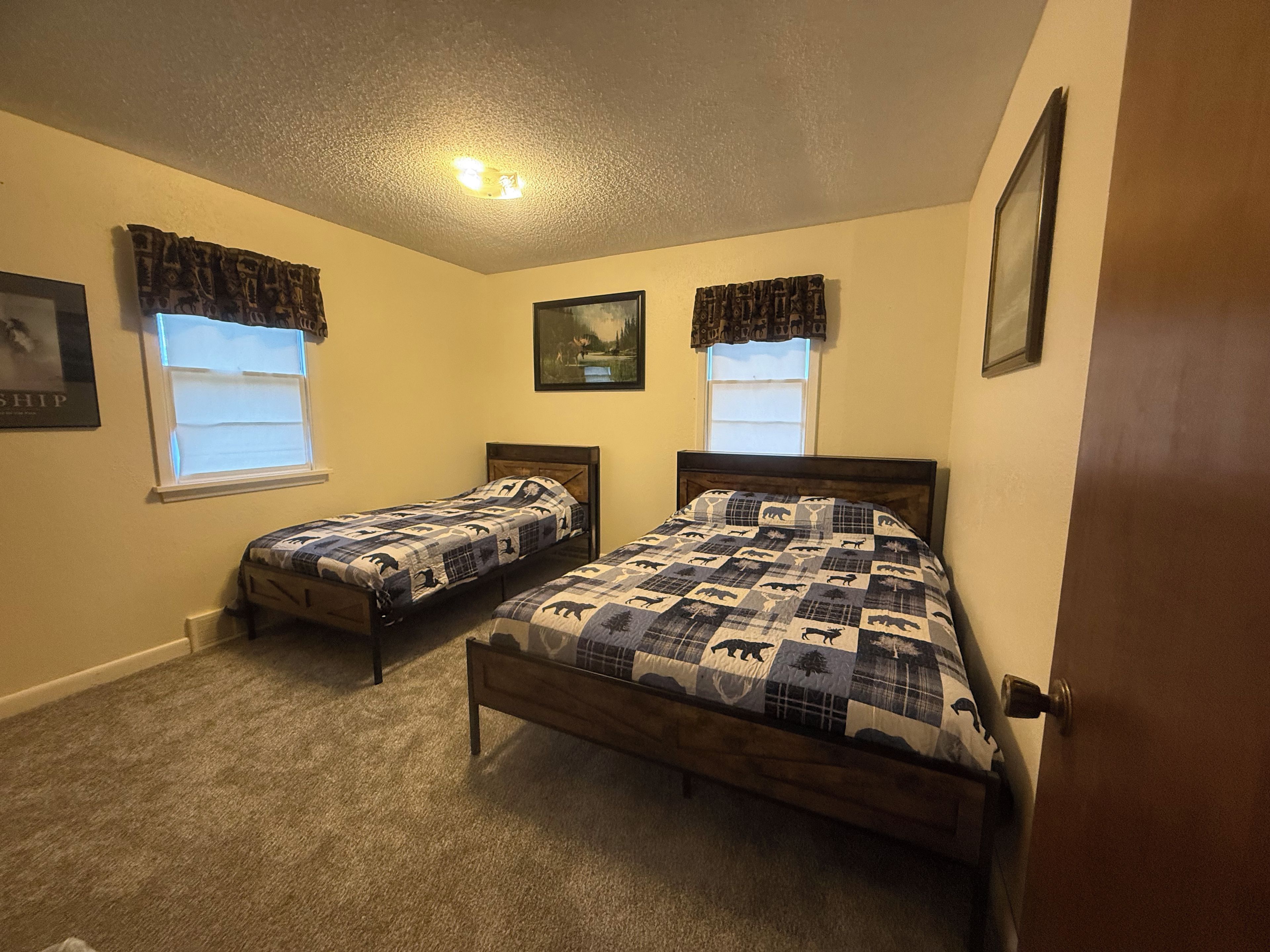 A bedroom with two single beds, a ceiling light, and windows with curtains.