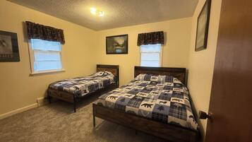 A bedroom with two single beds, a ceiling light, and windows with curtains.