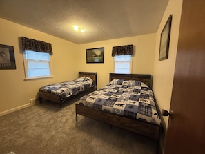 A bedroom with two single beds, a ceiling light, and windows with curtains.
