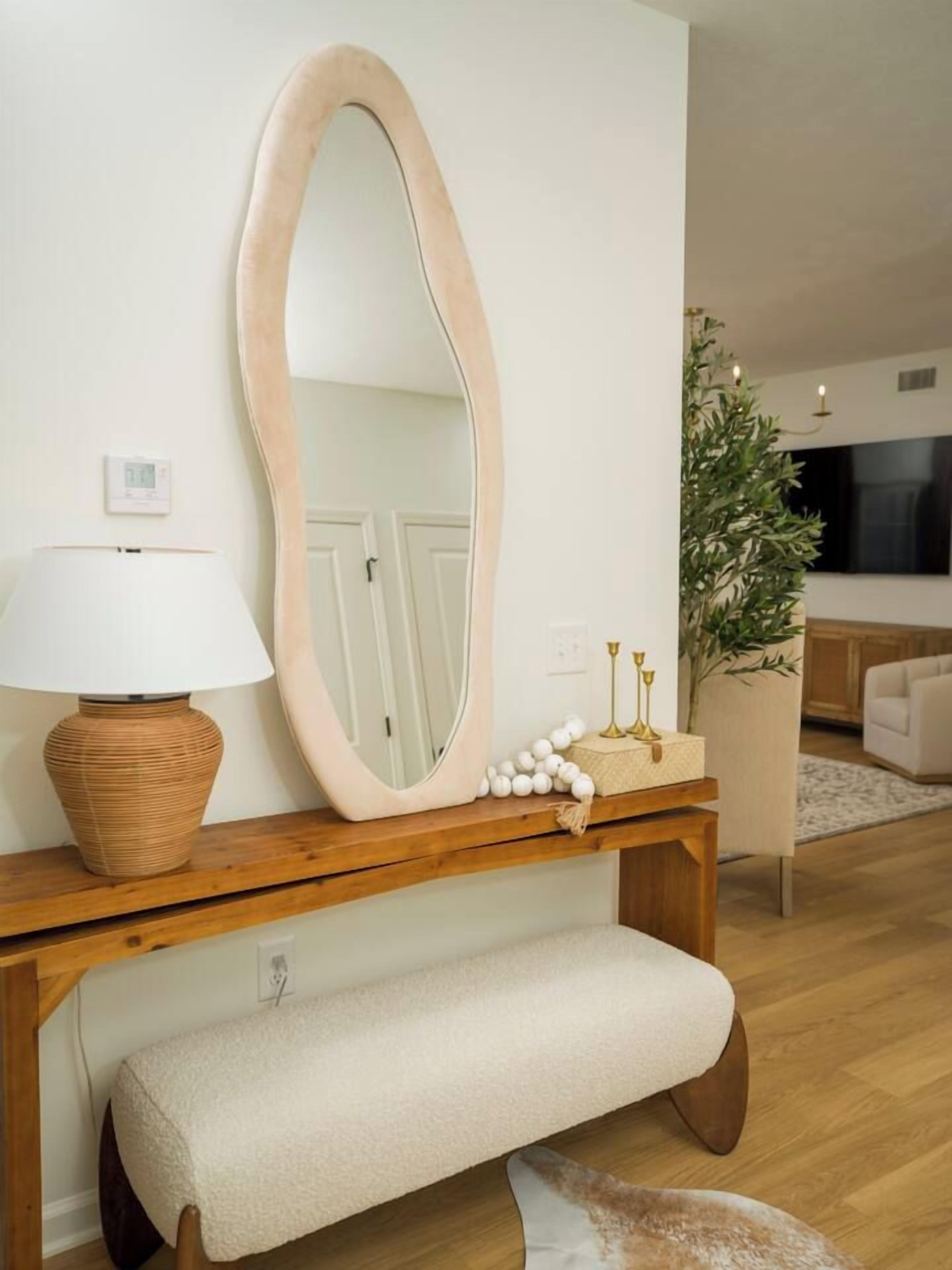 A wooden console table with a large oval mirror, a lamp, and decorative items.