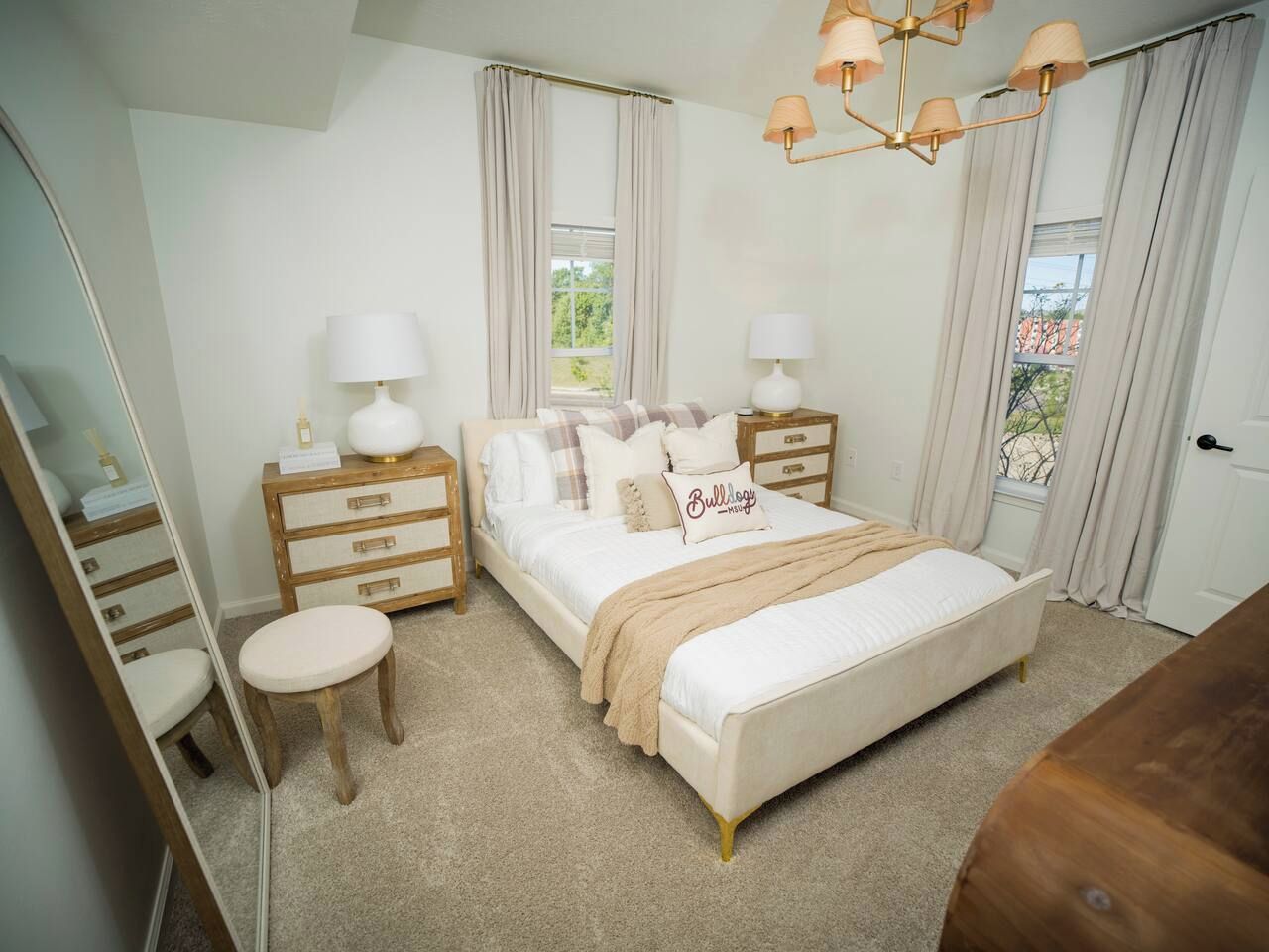 A bedroom with a bed, bedside tables, a mirror, and a window.