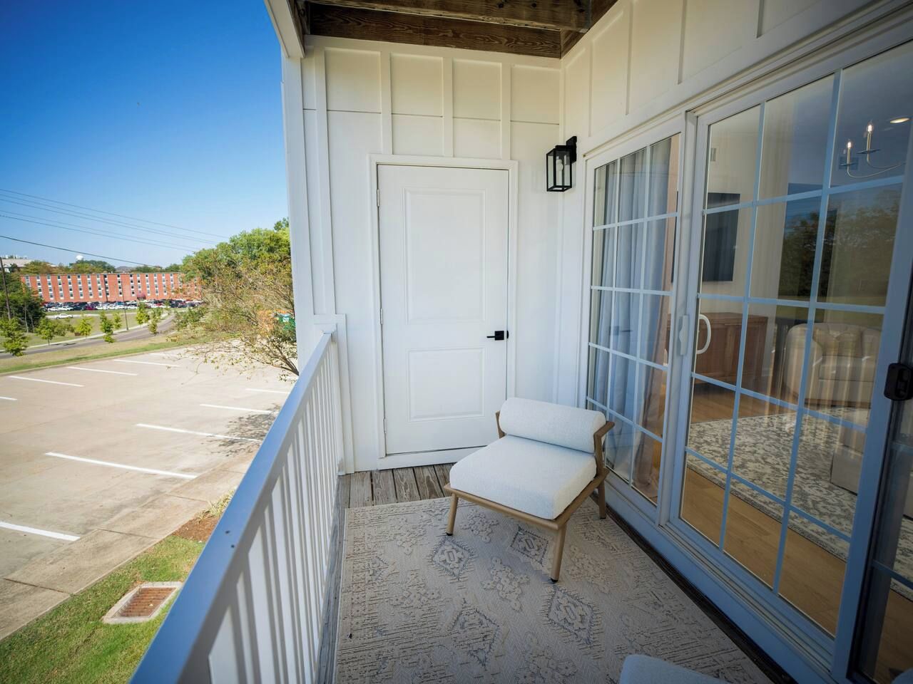 Un balcon avec une chaise blanche, une porte et une porte-fenêtre donnant sur un espace intérieur.
