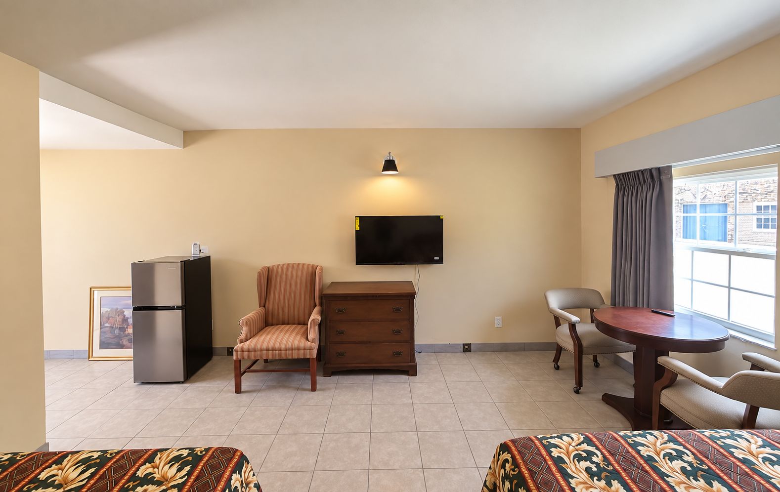 Une chambre d’hôtel équipée d’un lit, d’un bureau, d’une chaise, d’une télévision, d’un réfrigérateur et d’une fenêtre avec des rideaux.