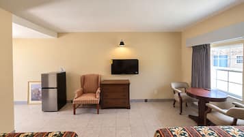 A hotel room with a bed, a desk, a chair, a television, a refrigerator, and a window with curtains.