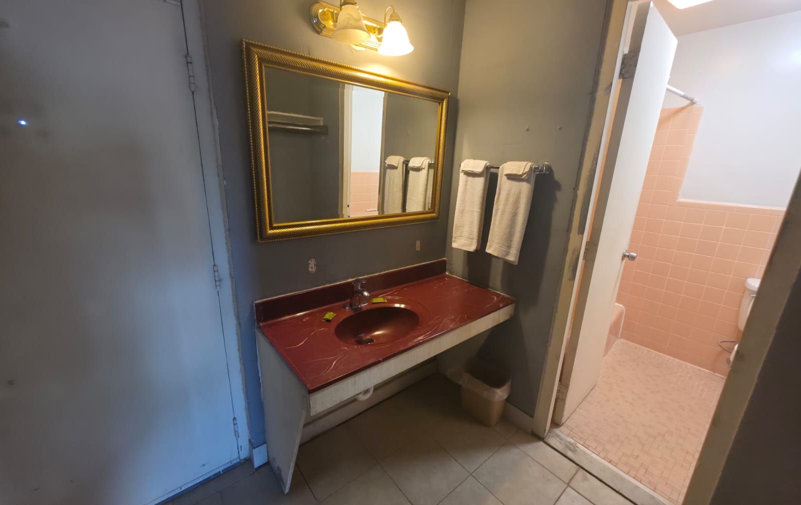 Een badkamer met een marmeren wastafel, een grote spiegel met gouden lijst en twee handdoeken aan de muur.