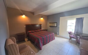 A bedroom with a bed, a desk, a chair, and a window.