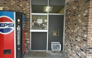 A brick building with a glass door entrance, a Pepsi vending machine, and a small air conditioning unit.