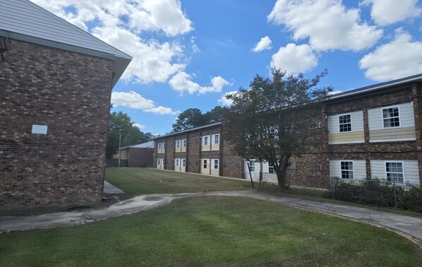 A brick building with a flat roof, a grassy lawn, and a clear sky with clouds.