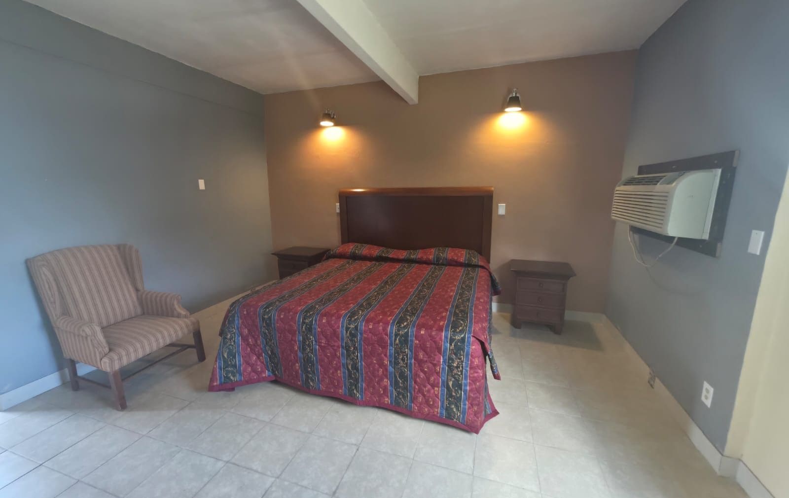 Un dormitorio con una cama, una silla, una mesita de noche y un aire acondicionado.