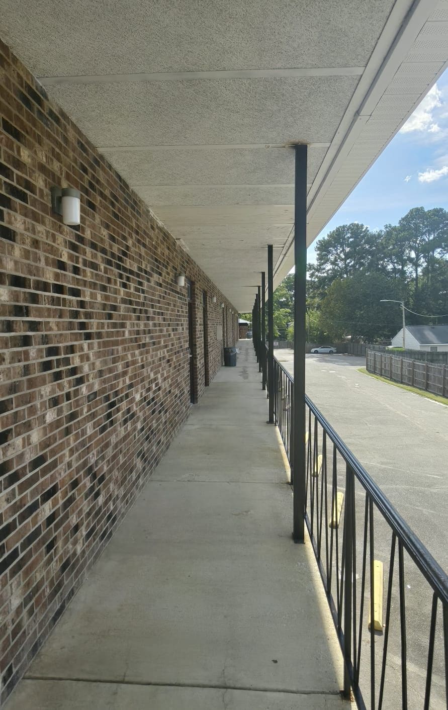 A covered walkway with a brick wall on one side and a metal railing on the other.