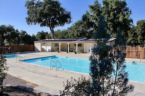 A swimming pool with a covered area, lounge chairs, and a wooden fence.