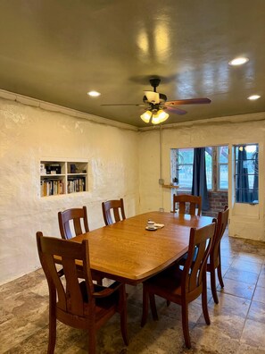 A dining area with a wooden table and chairs, a ceiling fan, and a bookshelf.