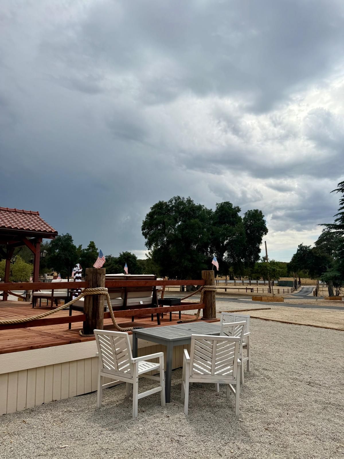 Un espacio al aire libre con mesas, sillas, una terraza de madera y un pabellón.