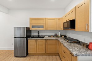Eine moderne Küche mit Holzausstattung, einem Edelstahlkühlschrank, einer Granitarbeitsplatte und einer Mikrowelle.