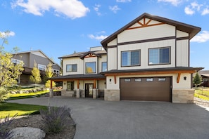 A two-story house with a garage, stone foundation, and a well-maintained lawn.