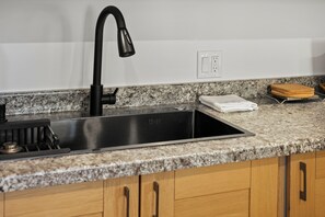 A kitchen with a stainless steel sink, a black faucet, granite countertop, wooden cabinets, and a towel rack. - Cute & new apartment near EGE airport -Vail Valley (Gypsum)