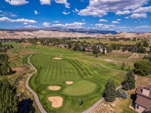 A golf course with a clear sky, surrounded by residential houses and mountains.