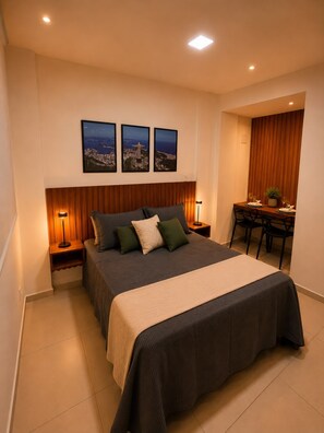 A hotel room with a large bed, bedside tables with lamps, a dining area with a table and chairs, and three framed pictures on the wall. - Estúdio Moderno a 50m Metrô Catete Perto da Praia (Rio de Janeiro)