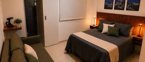 A modern bedroom with a bed, a sofa, an air conditioning unit, and a door leading to a bathroom.