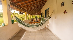 A covered outdoor area with a hammock, a table with chairs, and potted plants. - Casa com 2 Quartos Varanda e Rede no Bela Vista (Itariri)