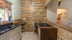 A kitchen with a gas stove, a sink, and a window with a view of greenery. - Casa com 2 Quartos Varanda e Rede no Bela Vista (Itariri)