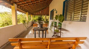 A covered outdoor seating area with benches, a table, and potted plants. - Casa com 2 Quartos Varanda e Rede no Bela Vista (Itariri)