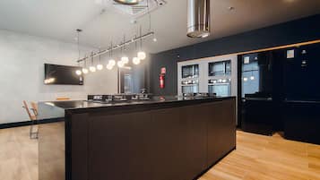 Una cucina moderna con isola centrale, forni integrati e illuminazione a sospensione.