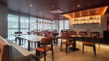 A modern dining area with multiple tables and chairs, large windows, and a kitchen area with shelves.